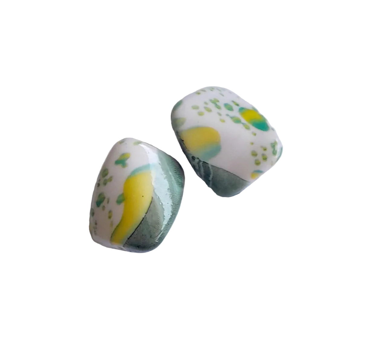 Two plastic beads with a white base, yellow and green abstract swirls, and green speckles, displayed on a clean white surface.