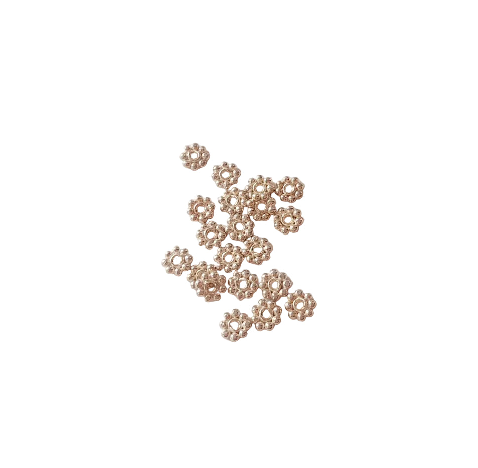Small decorative sterling silver metal flowers on a light pink background