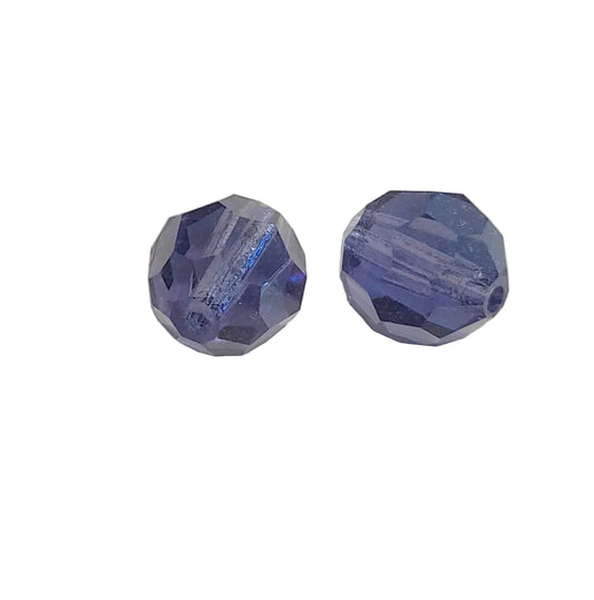 Two faceted blue glass beads with a central hole, displayed on a light beige surface.