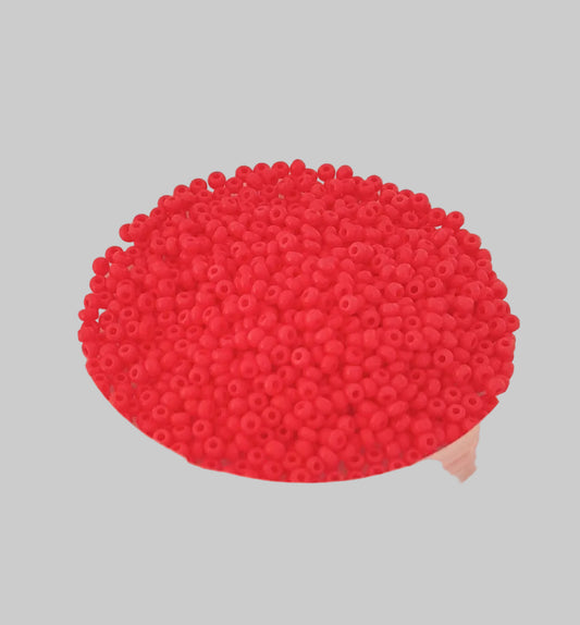 Bright coral seed beads piled in a clear round plastic container against a plain off-white background.