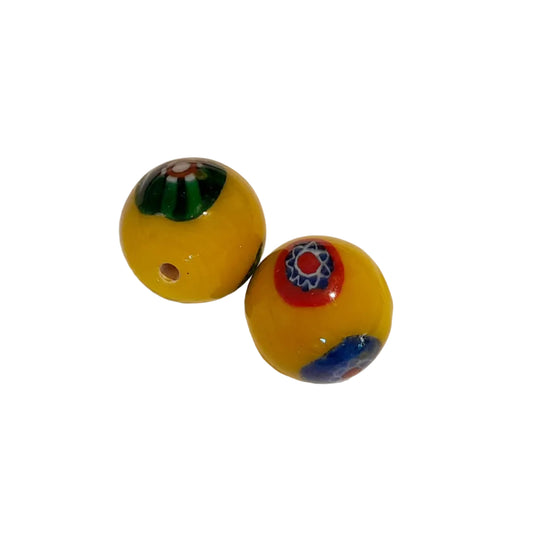 Two round yellow glass beads with colorful Millefiori patterns, one showing a green and red design and the other a red, white, blue, and green design,