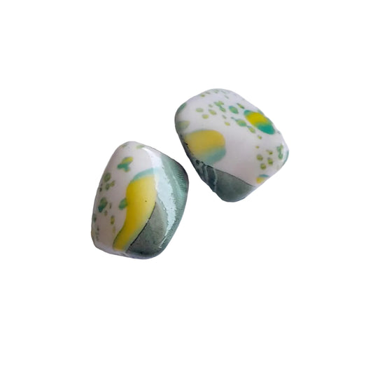 Two plastic beads with a white base, yellow and green abstract swirls, and green speckles, displayed on a clean white surface.