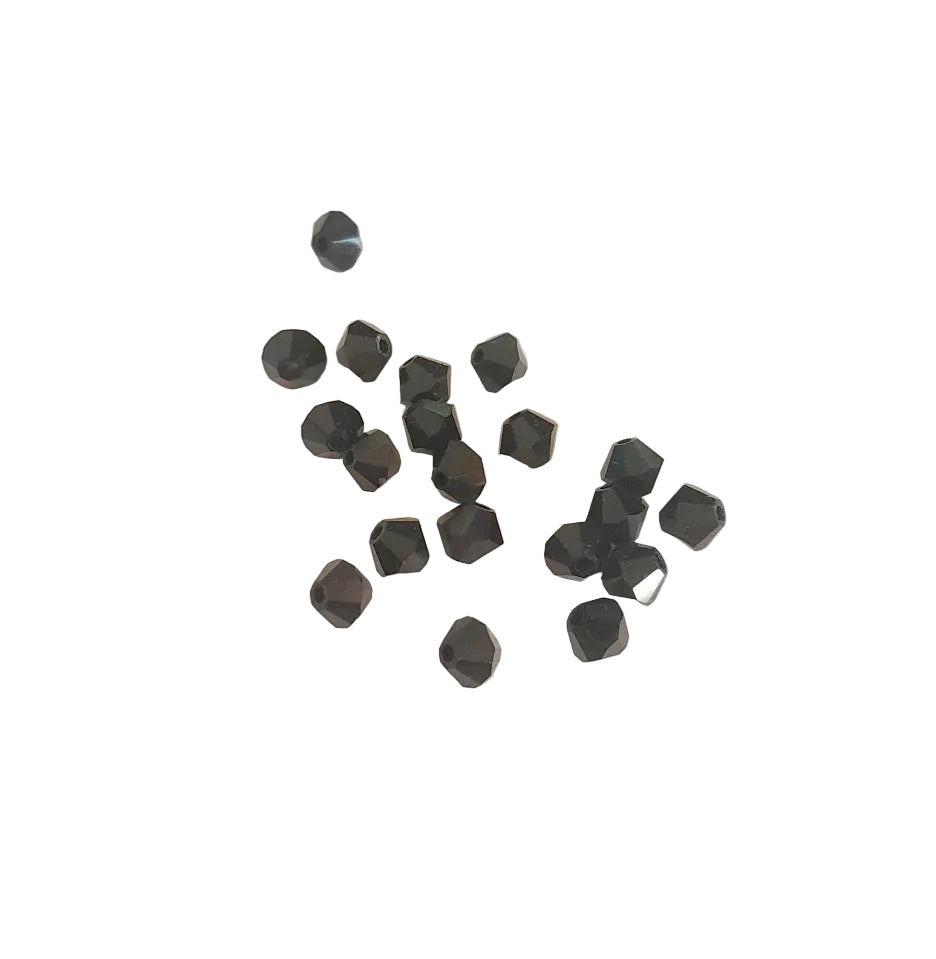 A group of small faceted black beads scattered on a light beige textured surface.
