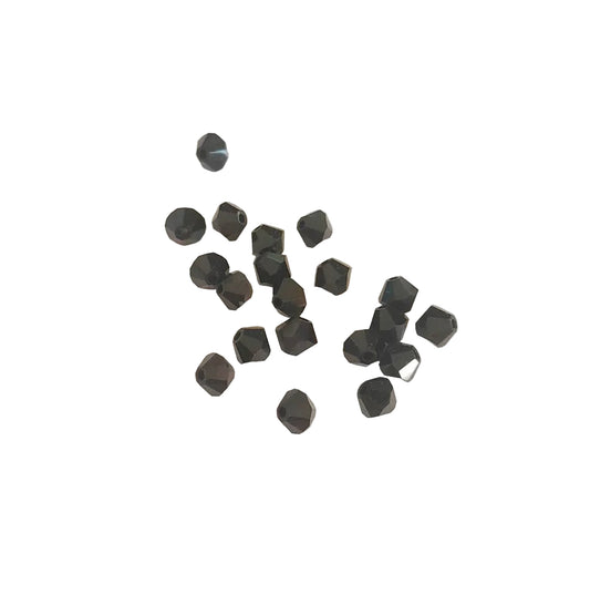 A group of small faceted black beads scattered on a light beige textured surface.