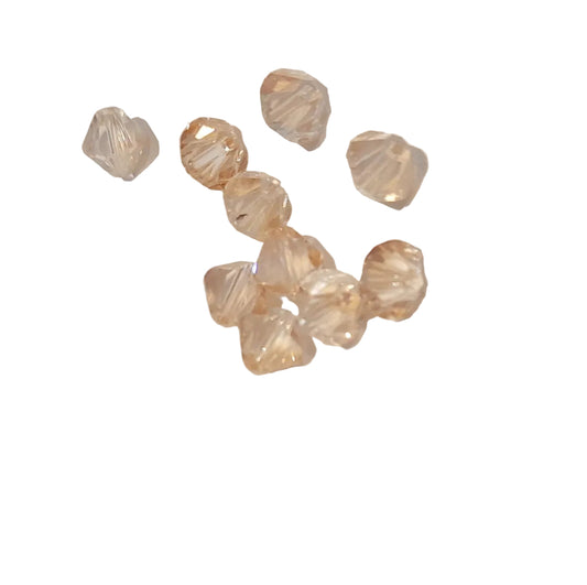 A group of small faceted clear beads with a warm champagne or pale peach tint, scattered on a plain light background.