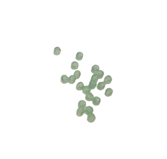 A small cluster of faceted light green glass beads scattered on a plain off-white background.