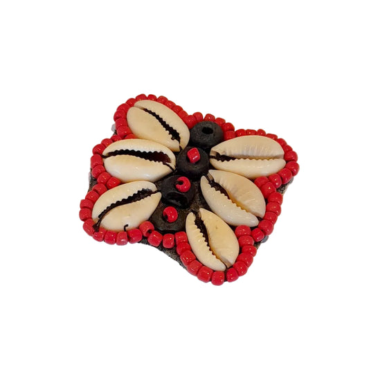 A butterfly-shaped decorative brooch featuring six cream cowrie shells, a border of red beads, and a butterfly element with small red beads, 