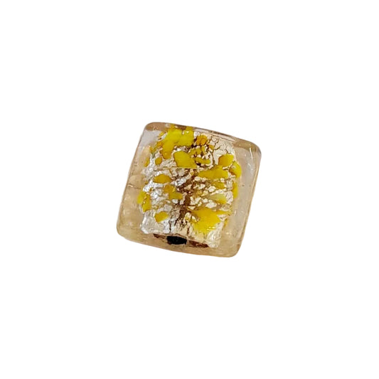 A square glass bead with a clear, slightly warm tint containing yellow and silver foil flecks, 
