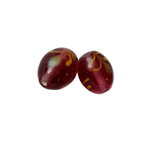Two oval glass beads with a deep red translucent body and yellow swirl patterns