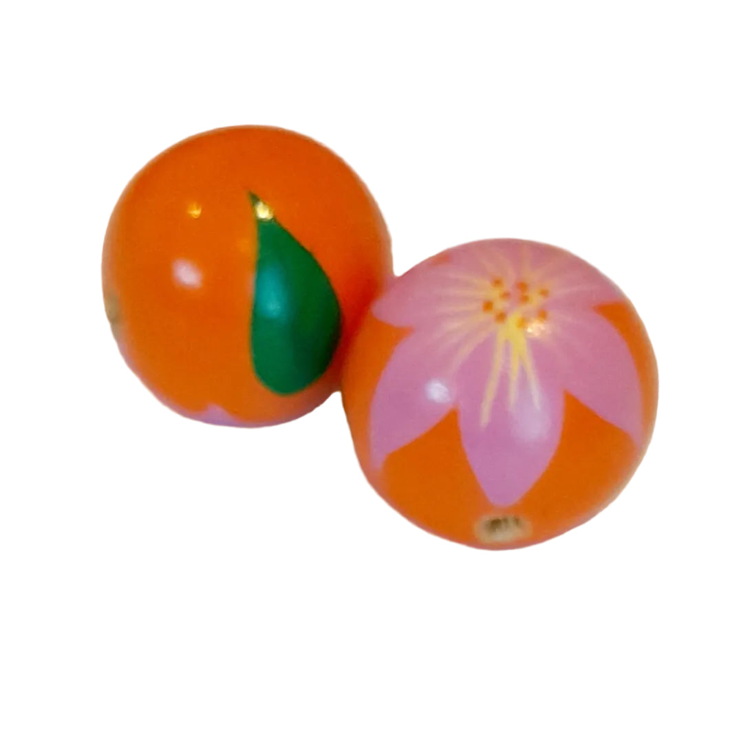 Two round orange wooden beads with hand-painted designs, one featuring a green leaf and the other a pink flower, baby blessing beads