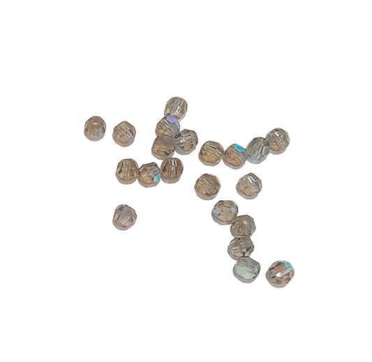 A group of small faceted glass beads with a gray and silver iridescent finish, scattered on a plain off-white background.