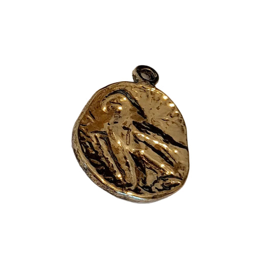 A small irregularly shaped gold pendant with a dark oxidized recessed design, featuring a small top loop,