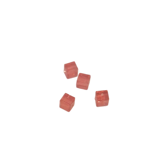 Four small translucent pinkish-red cube-shaped beads arranged on a plain light background.