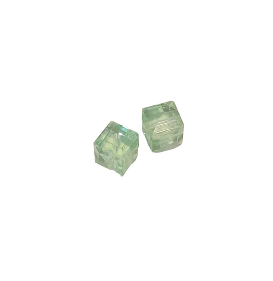 Two small translucent light green cube-shaped beads on a plain off-white background.