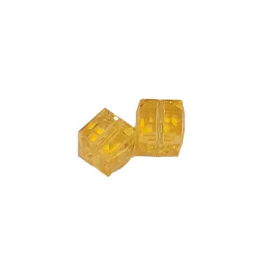 Two small translucent yellow cube-shaped beads standing upright on a plain off-white surface.